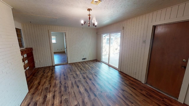 interior space with an inviting chandelier, dark wood-type flooring, wood walls, and a textured ceiling