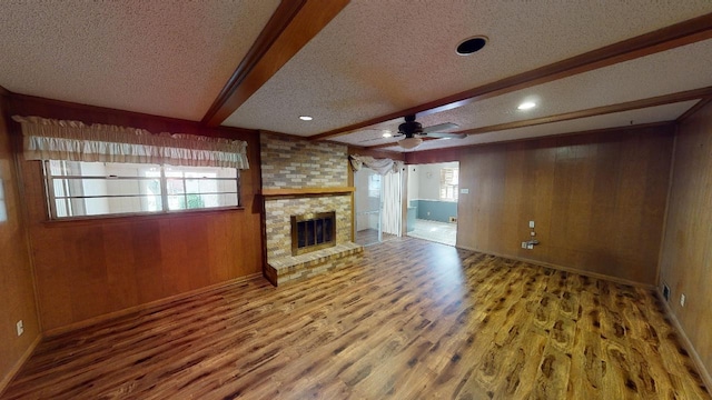 unfurnished living room with beam ceiling, a brick fireplace, wooden walls, and a textured ceiling