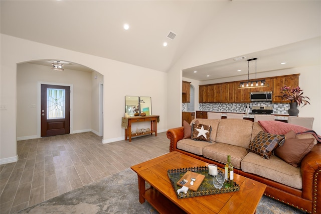 living room featuring arched walkways, recessed lighting, visible vents, light wood-type flooring, and baseboards