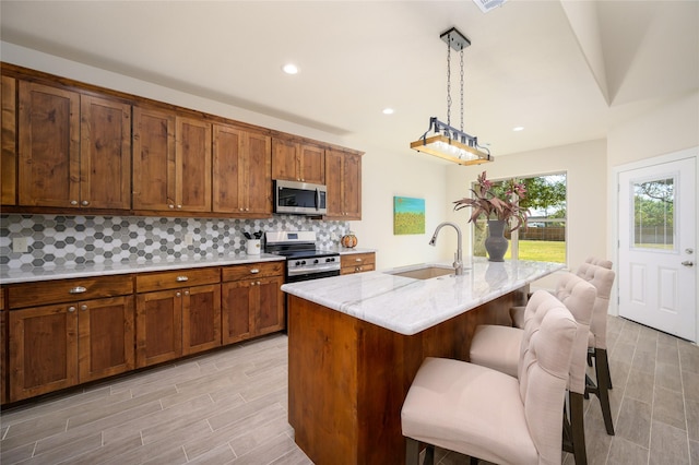 kitchen featuring a kitchen breakfast bar, decorative light fixtures, a sink, stainless steel appliances, and backsplash