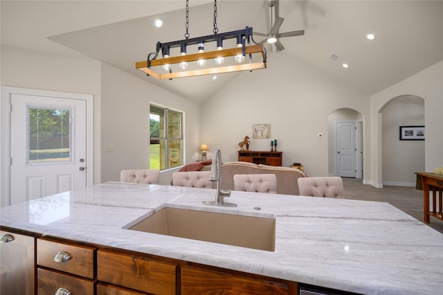 kitchen featuring arched walkways, a sink, visible vents, open floor plan, and light stone countertops