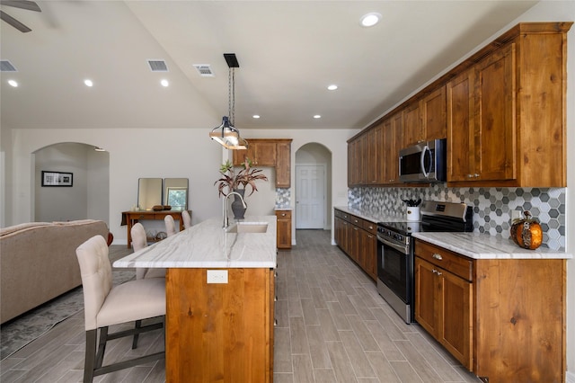 kitchen with arched walkways, stainless steel appliances, a sink, visible vents, and decorative backsplash