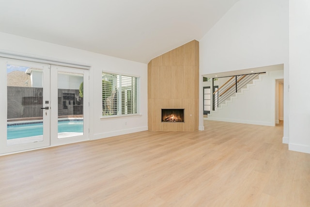 unfurnished living room with french doors, lofted ceiling, a tiled fireplace, and light hardwood / wood-style flooring