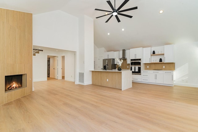 unfurnished living room with ceiling fan, high vaulted ceiling, a large fireplace, and light hardwood / wood-style floors