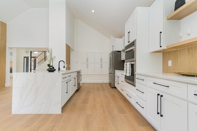 kitchen featuring appliances with stainless steel finishes, sink, white cabinets, light stone counters, and light hardwood / wood-style floors