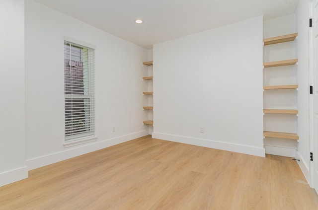 unfurnished room with built in shelves and light wood-type flooring