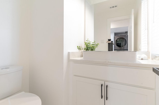 bathroom featuring stacked washer / dryer, toilet, and vanity