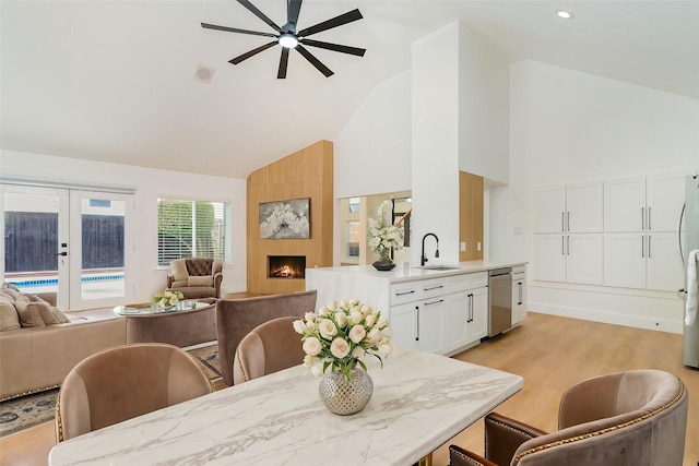 dining room featuring high vaulted ceiling, a fireplace, sink, light hardwood / wood-style floors, and french doors