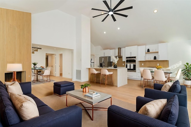 living room with ceiling fan, high vaulted ceiling, and light wood-type flooring