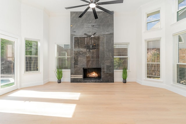 unfurnished living room with a tile fireplace, ornamental molding, and light hardwood / wood-style flooring