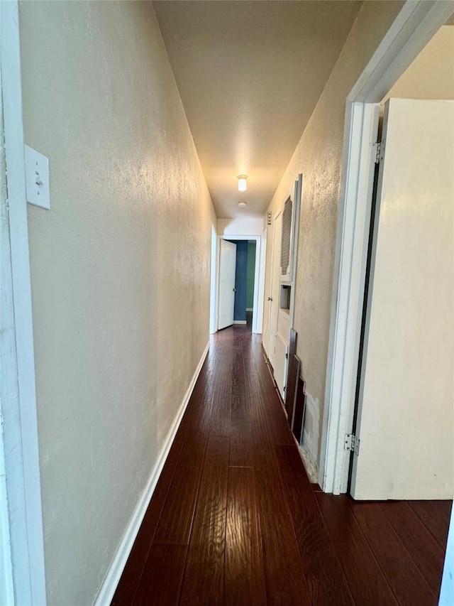 hallway featuring dark wood-style floors, a textured wall, and baseboards