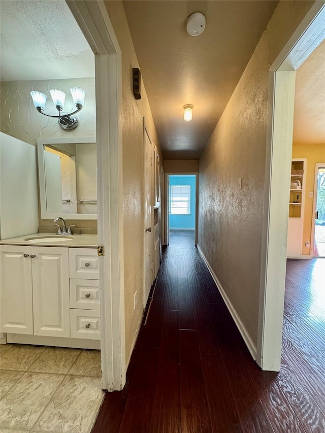 hallway featuring a textured wall, a sink, baseboards, and hardwood / wood-style flooring