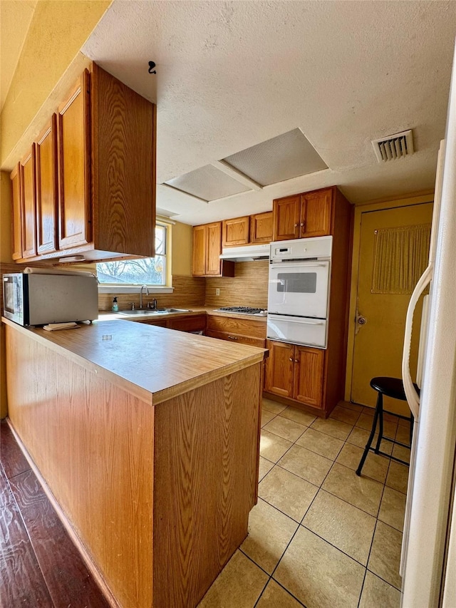 kitchen featuring a warming drawer, visible vents, a sink, white appliances, and under cabinet range hood