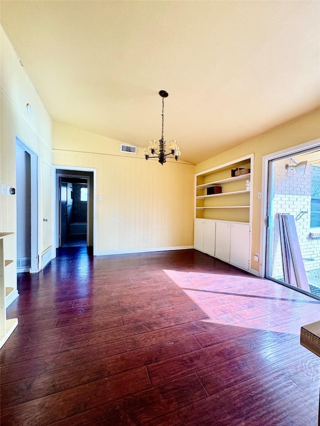 spare room with built in shelves, a notable chandelier, dark wood-style flooring, visible vents, and baseboards