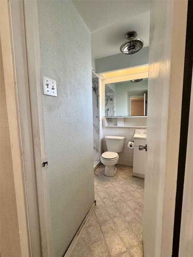 bathroom featuring toilet, a textured wall, tile walls, and vanity