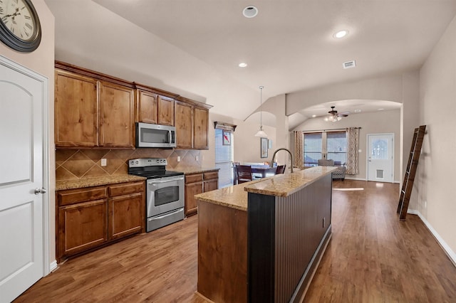 kitchen featuring appliances with stainless steel finishes, tasteful backsplash, an island with sink, vaulted ceiling, and ceiling fan