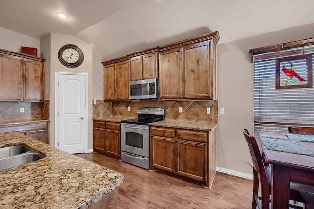 kitchen with light stone countertops, lofted ceiling, stainless steel appliances, backsplash, and light hardwood / wood-style flooring