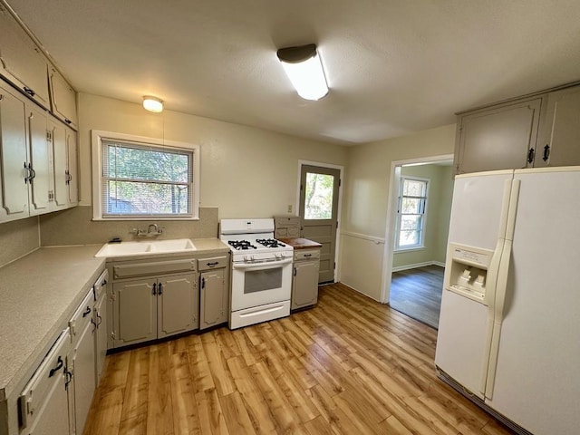 kitchen with a wealth of natural light, sink, light hardwood / wood-style floors, and white appliances