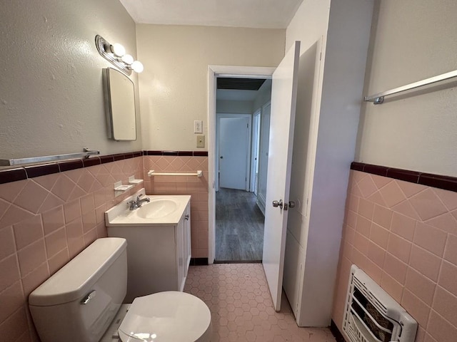 bathroom with toilet, vanity, tile walls, tile patterned flooring, and heating unit