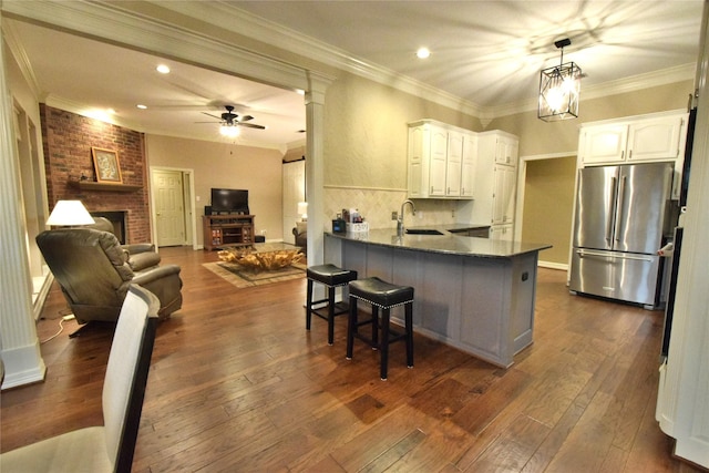 kitchen with white cabinetry, kitchen peninsula, a brick fireplace, stainless steel refrigerator, and sink