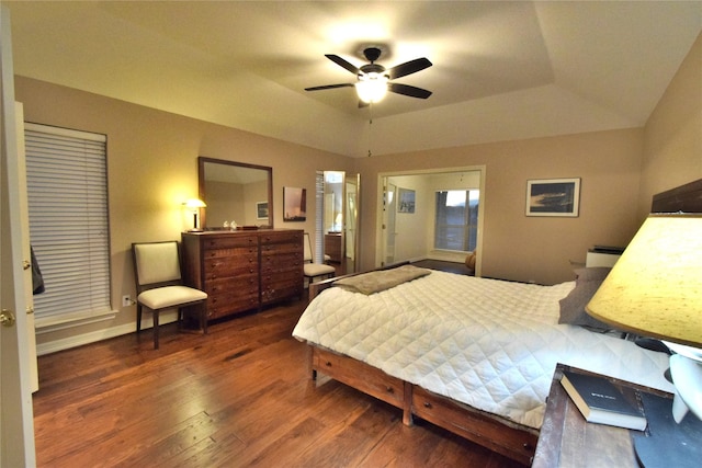 bedroom with ceiling fan, vaulted ceiling, dark wood-type flooring, and a tray ceiling