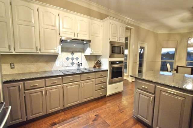 kitchen featuring appliances with stainless steel finishes, white cabinetry, dark hardwood / wood-style flooring, dark stone countertops, and decorative backsplash