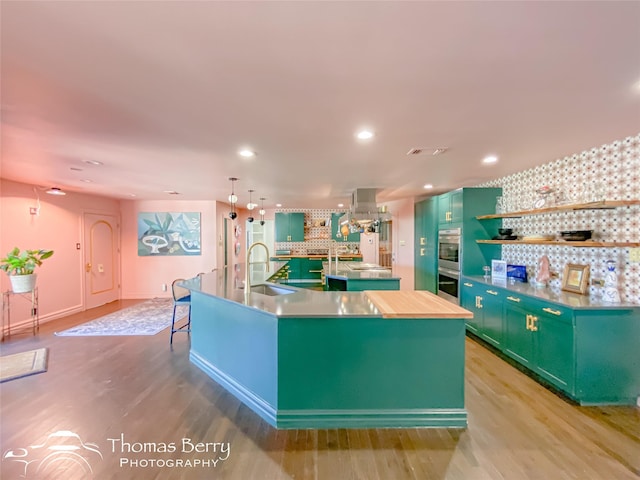 kitchen featuring green cabinets, sink, light hardwood / wood-style floors, and a kitchen island with sink