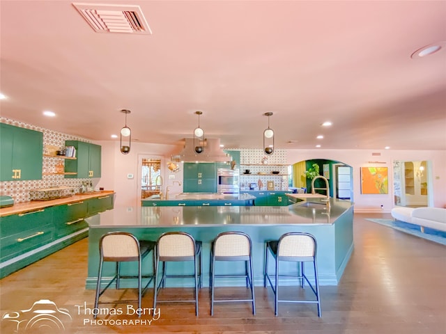 kitchen with backsplash, a spacious island, a breakfast bar, green cabinets, and hanging light fixtures