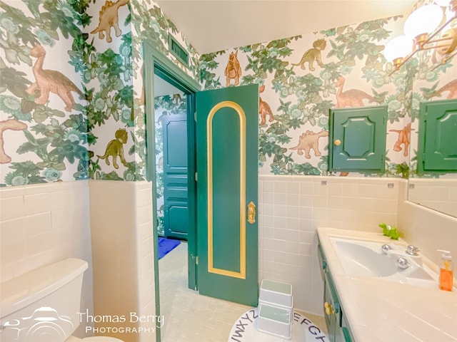 bathroom with toilet, vanity, and tile walls