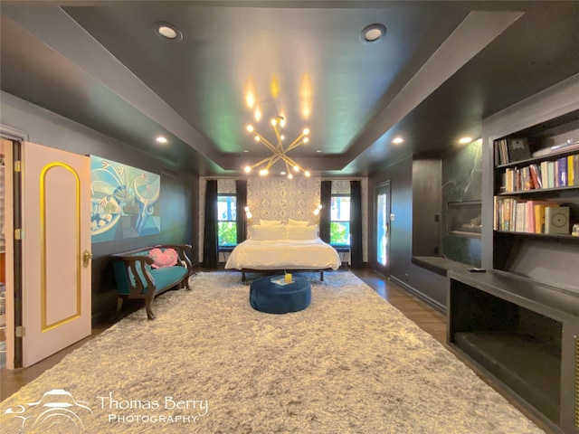 bedroom with a raised ceiling, dark hardwood / wood-style floors, and a notable chandelier