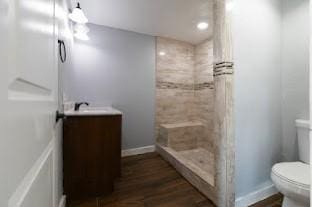 bathroom with toilet, a tile shower, wood-type flooring, and vanity