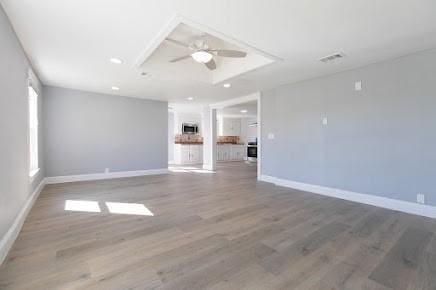 unfurnished living room with ceiling fan, a raised ceiling, and hardwood / wood-style flooring