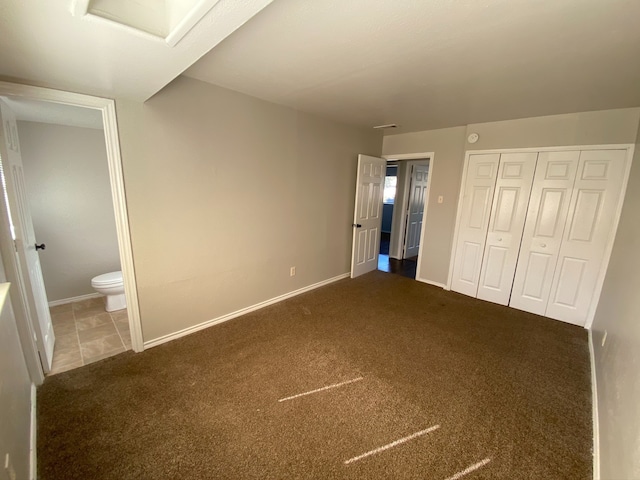 unfurnished bedroom with connected bathroom, dark carpet, and a closet