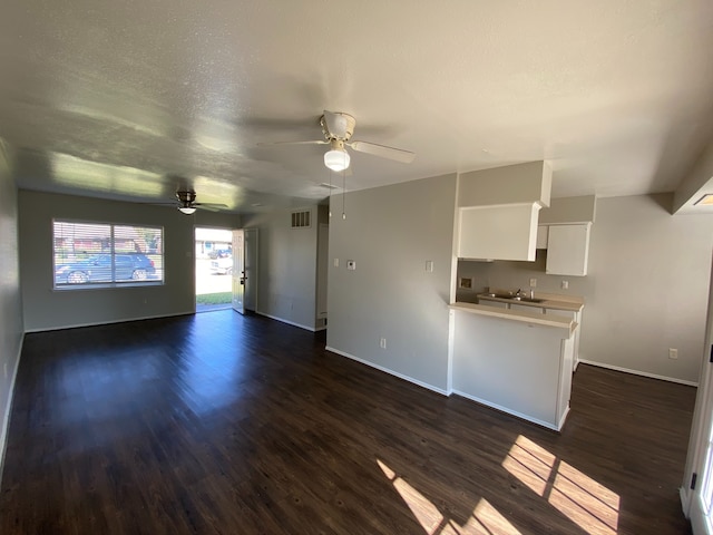 unfurnished living room with ceiling fan, dark hardwood / wood-style flooring, and a textured ceiling