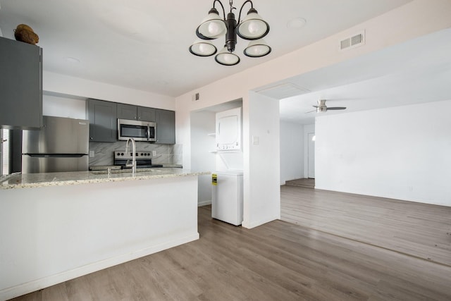 kitchen featuring ceiling fan with notable chandelier, light stone countertops, stainless steel appliances, decorative backsplash, and gray cabinets