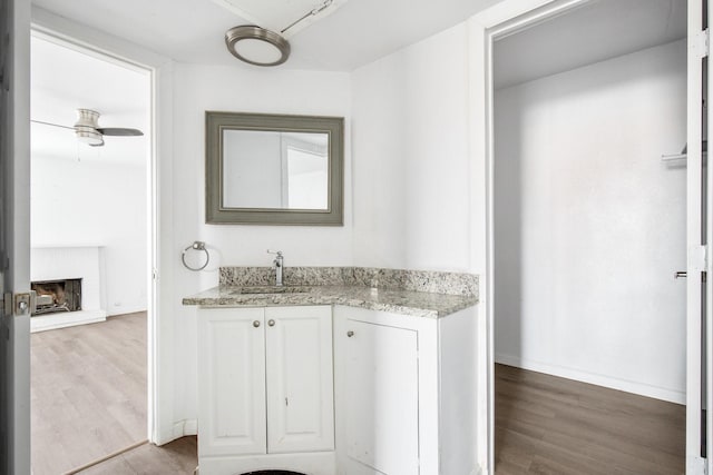 bathroom with vanity, ceiling fan, hardwood / wood-style flooring, and a brick fireplace