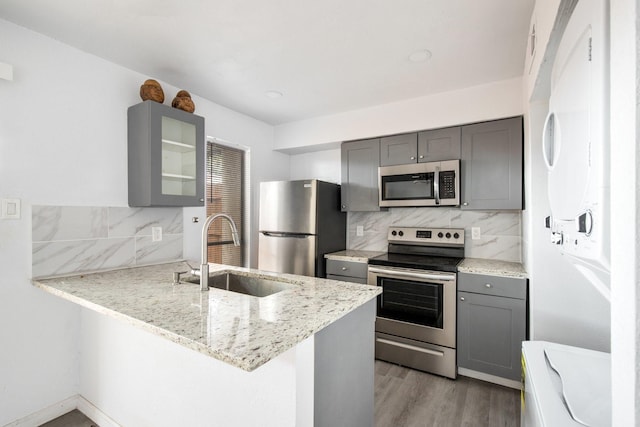 kitchen featuring light stone countertops, appliances with stainless steel finishes, kitchen peninsula, and sink