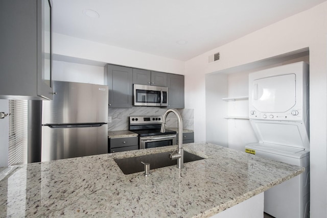 kitchen featuring light stone countertops, backsplash, stainless steel appliances, and stacked washer and dryer