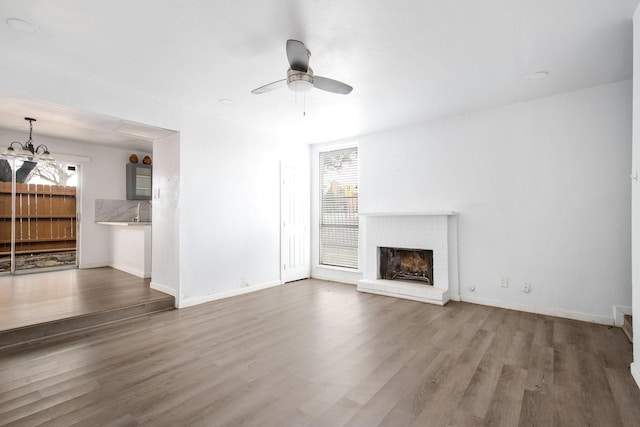 unfurnished living room featuring a fireplace, a wealth of natural light, ceiling fan with notable chandelier, and hardwood / wood-style flooring