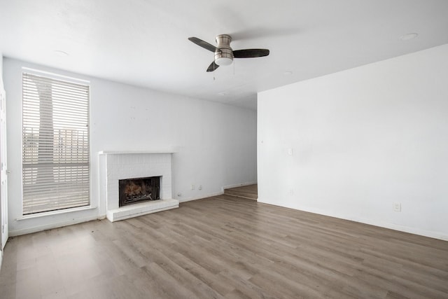 unfurnished living room with ceiling fan, light wood-type flooring, and a brick fireplace