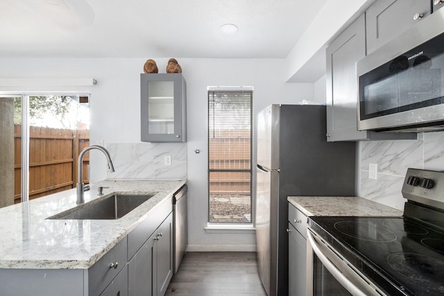 kitchen with appliances with stainless steel finishes, sink, backsplash, light stone counters, and gray cabinetry