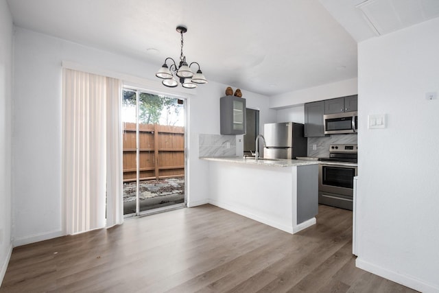 kitchen featuring appliances with stainless steel finishes, tasteful backsplash, gray cabinets, kitchen peninsula, and a chandelier