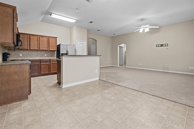 kitchen with arched walkways, light colored carpet, open floor plan, stainless steel refrigerator with ice dispenser, and brown cabinets