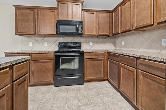 kitchen featuring light tile patterned floors, light stone counters, backsplash, brown cabinets, and black appliances