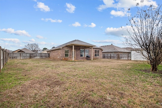 back of house with a fenced backyard, a lawn, and brick siding