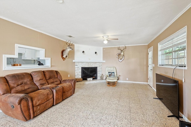 living room with ceiling fan, a stone fireplace, and ornamental molding