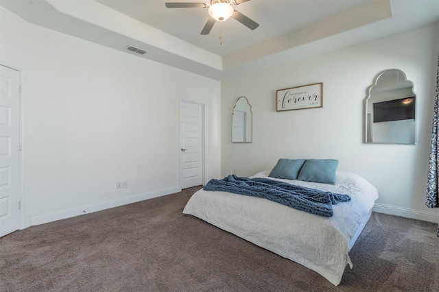 bedroom featuring ceiling fan, dark carpet, and a raised ceiling