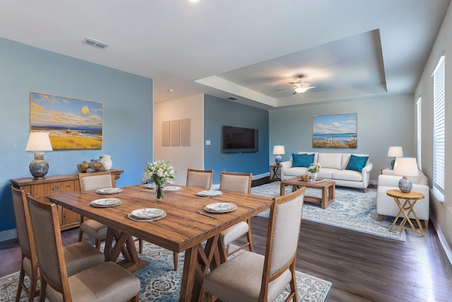 dining space featuring a raised ceiling, ceiling fan, and dark wood-type flooring