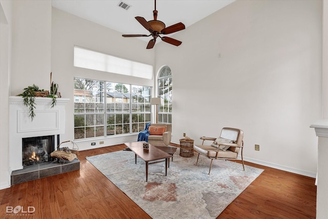 sitting room featuring ceiling fan, a towering ceiling, wood-type flooring, and a tile fireplace