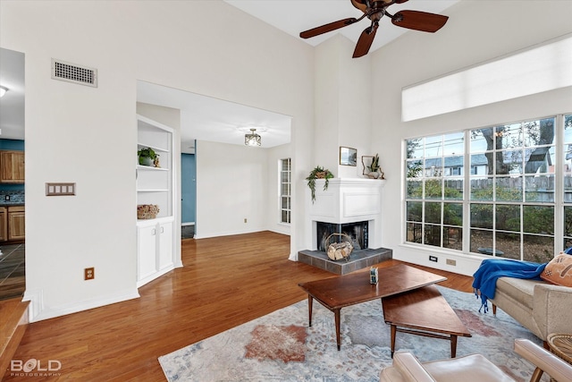 living room featuring ceiling fan, built in shelves, a fireplace, and hardwood / wood-style flooring